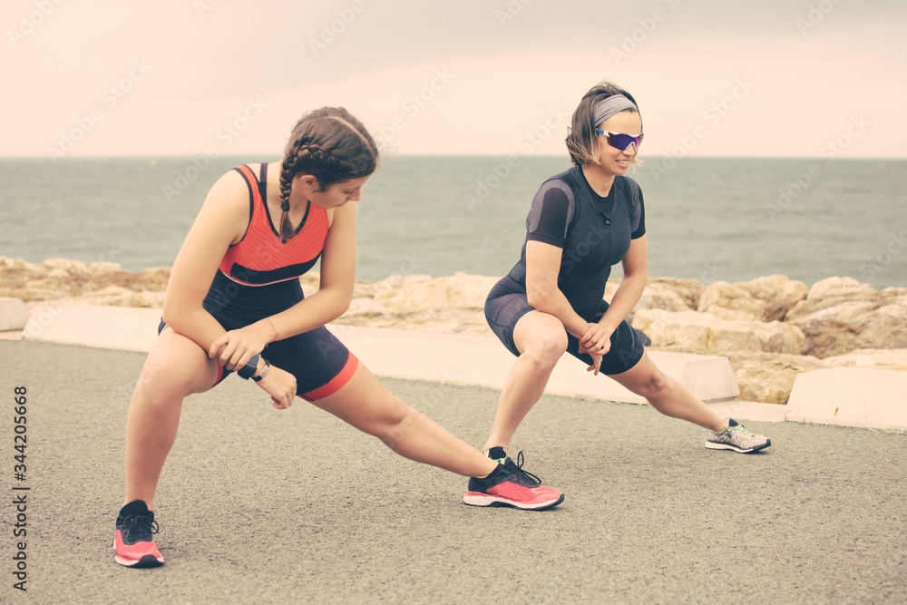 Athletic women stretching near sea. Full length view of sporty women in sportswear stretching and working out on sea coast. Triathlon concept