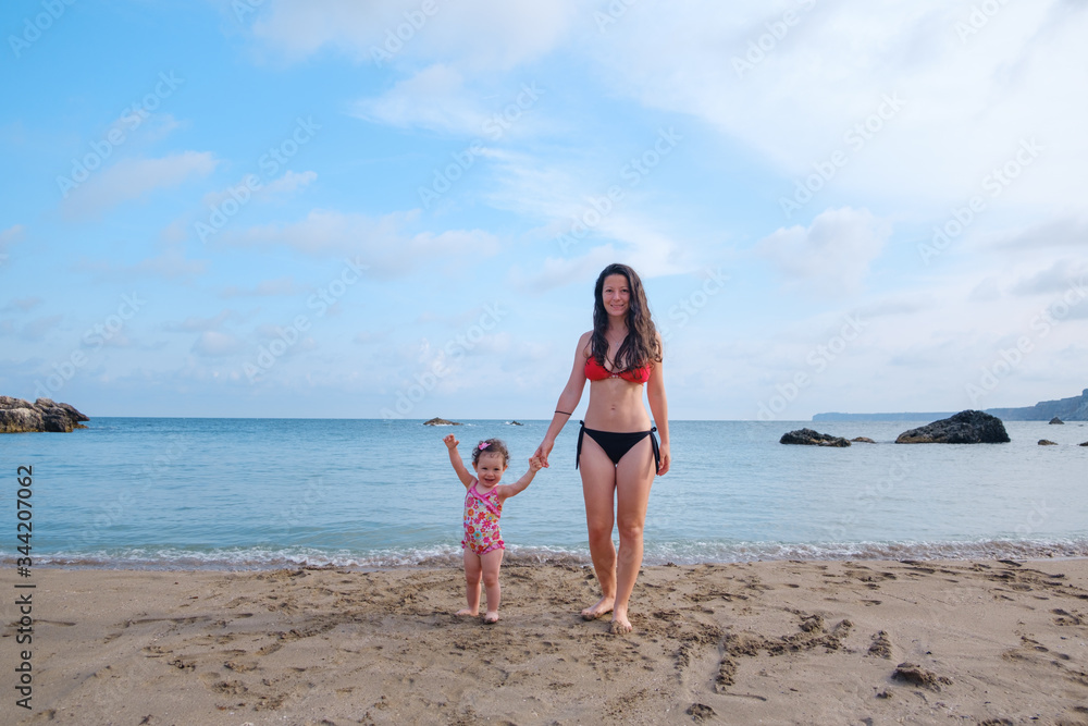 Wide Angle portrait of Happy Little Girl and Young Woman on the Beach with beautiful blue water and sky in the Background Wide Angle portrait of Happy Little Girl and Young Woman on the Beach with beautiful blue water and sky in the Background