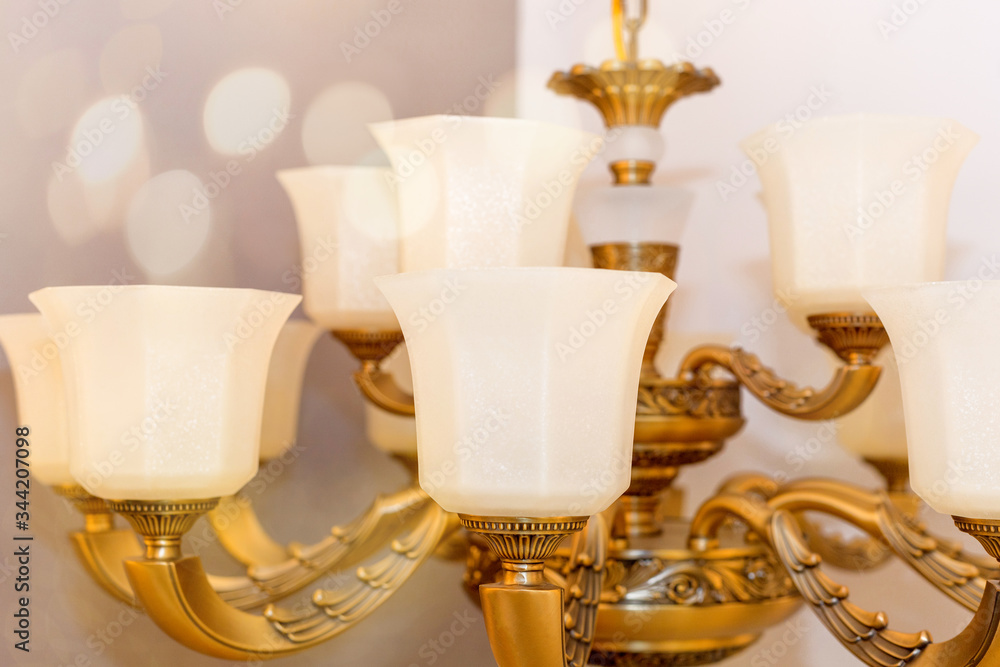 Image of a ceiling chandelier with white frosted plafonds mounted on a gold-colored armature in the room. For classic interior. Bokeh. Close up. Soft warm filter, selective focus.