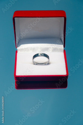 A groom's wedding ring in a red box on a reflected blue sky background