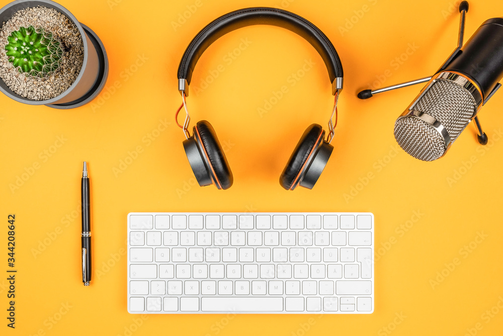 podcasting and podcast recording concept, top view of microphone, headphones and computer keyboard on orange desk