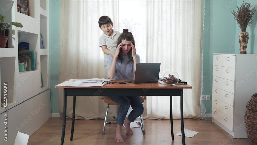 Parent working from home. Remote work. Family on self-isolation. Home office. A woman is working at a table. The son interferes with the mother's work. Mom gets annoyed. Quarantine. Epidemic. Crisis. Parent working from home. Remote work. Family on self-isolation. Home office. A woman is working at a table. The son interferes with the mother's work. Mom gets annoyed. Quarantine. Epidemic. Crisis.