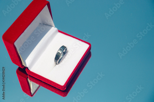 A groom's wedding ring in a red box on a reflected blue sky background