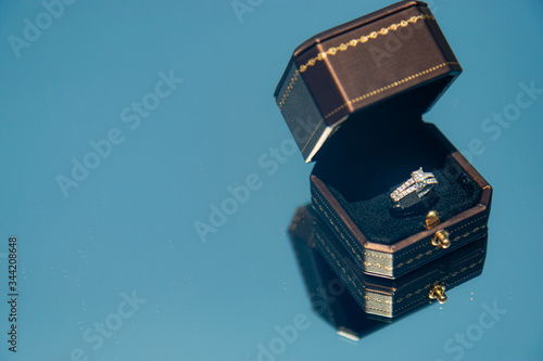 A bride's diamond wedding ring in a black box on a reflected blue sky background
