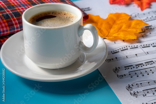 morning music composition. music notes and a cup of strong coffee on a blue background. autumn leaves on a sheet of paper with musical notes