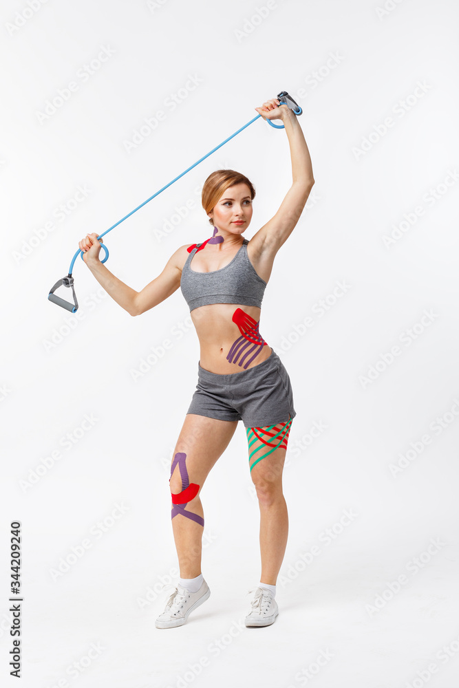 Kinesiology taping. Kinesiology tape on patient knee,hip, shoulder. Female athlete doing exercises with expender. Post traumatic rehabilitation,weight loss,cellulite removal, sport physical therapy. Kinesiology taping. Kinesiology tape on patient knee,hip, shoulder. Female athlete doing exercises with expender. Post traumatic rehabilitation,weight loss,cellulite removal, sport physical therapy.