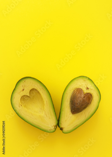Flat lay of cut in half avocado with seed in shape of heart on yellow background love forever inseparable concept