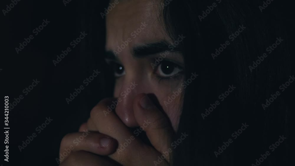 Closeup of a woman watching a scary movie in the dark with TV light reflections on her face. Closeup of a woman watching a scary movie in the dark with TV light reflections on her face.