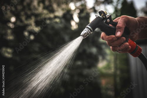 Watering garden equipment - hand holds the sprinkler hose for irrigation plants. Gardener hand with watering gun.