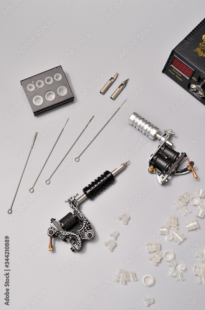 Fototapeta premium Tattoo machines, needles and all these tattoo stuff isolated on grey background. Tattoo guns. Pattern with tattoo machine, wallpaper for your business design