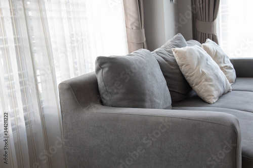 Close-up picture of grey soft with side pillows are comfortable, yet stylish and modern, for the whole family to spend their free time resting under the evening light that pass through the window. photo