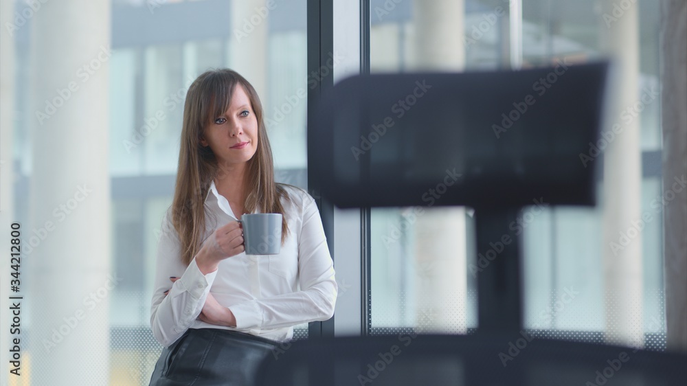 Businesswoman taking break in office drinking coffee standing in window and daydreaming, thinking. Businesswoman taking break in office drinking coffee standing in window and daydreaming, thinking.
