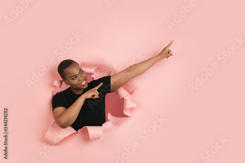 Pointing. Cheerful african-american young woman poses in torn coral paper background, emotional and expressive. Breaking on, breakthrought. Concept of human emotions, facial expression, sales, ad. © master1305