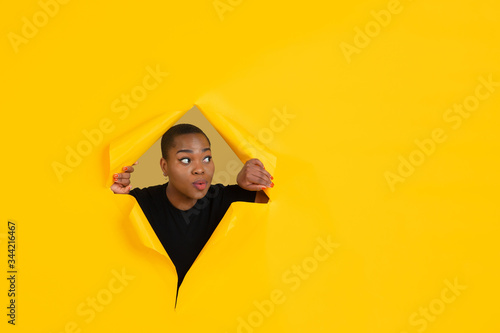 Wondered. Cheerful african-american young woman poses in torn yellow paper background, emotional and expressive. Breaking on, breakthrought. Concept of human emotions, facial expression, sales, ad. © master1305