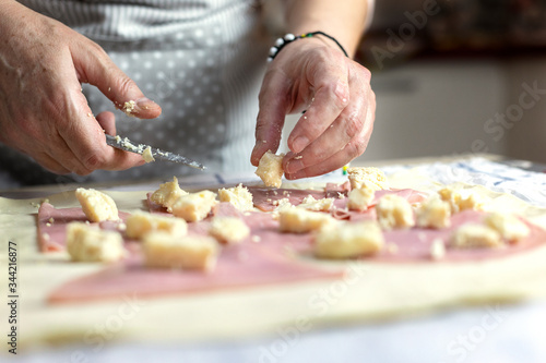 Female hands cutting cheese on raw puff pastry.