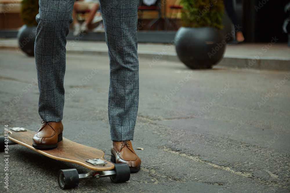 Fashionable European business man in perfect suite walk on the street, using skateboard longboard and suit man, coffee take away and smile me