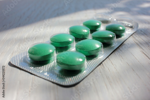Big round green pills in blister on white wooden background. Close-up. Copy space. Headache medicine
