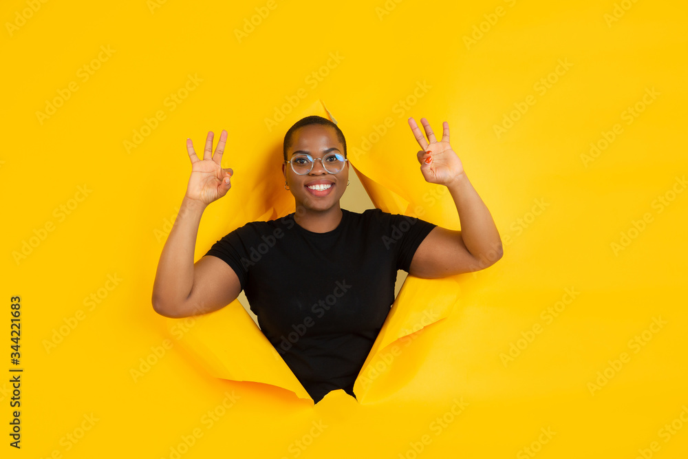 Nice gesture. Cheerful african-american young woman poses in torn yellow paper background, emotional and expressive. Breaking on, breakthrought. Concept of human emotions, facial expression, sales, ad Nice gesture. Cheerful african-american young woman poses in torn yellow paper background, emotional and expressive. Breaking on, breakthrought. Concept of human emotions, facial expression, sales, ad
