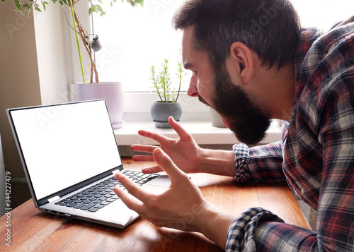 A man with a beard in a plaid shirt lost patience and screams at a laptop.