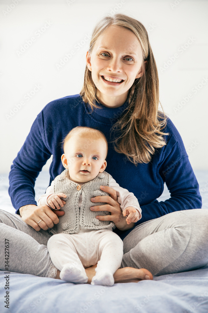 Happy beautiful new mom enjoying time with sweet little baby girl. Young woman nursing six month daughter in bedroom at home. Motherhood concept Happy beautiful new mom enjoying time with sweet little baby girl. Young woman nursing six month daughter in bedroom at home. Motherhood concept