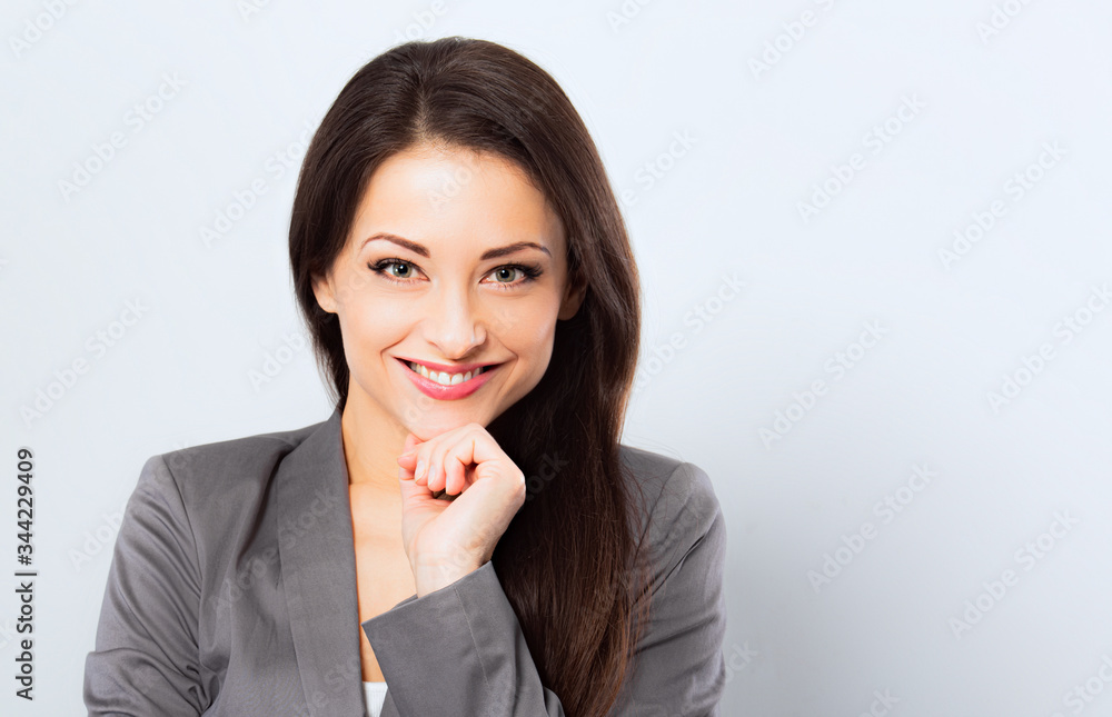 Beautiful smiling business woman in suit holding the hands under the face on blue background. Closeup Beautiful smiling business woman in suit holding the hands under the face on blue background. Closeup