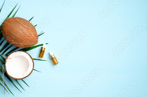 Coconut oil with half of coconut and palm leaf on blue background. Flat lay, top view. SPA natural organic cosmetic. Skin care, hair treatment concept