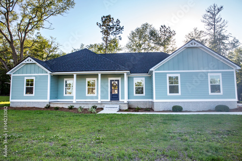 Front view of a brand new construction house with blue siding, a ranch style home with a yard © Ursula Page