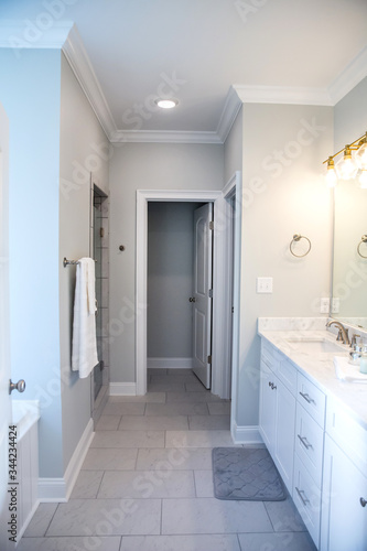 All white and gray modern contemporary master bathroom in a small new construction house with tiled floor, a vanity cabinet, double sinks and a mirror