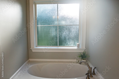 A white large garden style bathtub with a stainless silver faucet and a large frosted window with light coming through