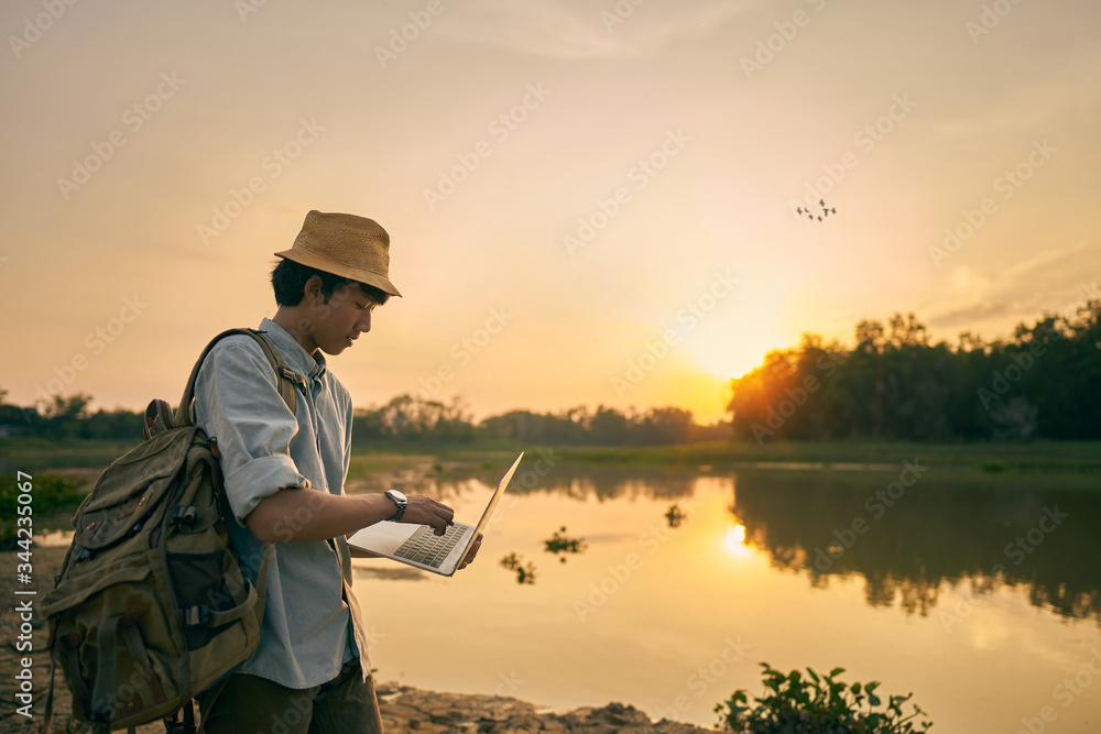 Fototapeta premium young man uses a laptop and the lake and nature at sunset
