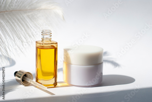 Yellow glass with creme Bottle mockup cosmetic oil on white background with soft feather Copy space. Beauty skin care