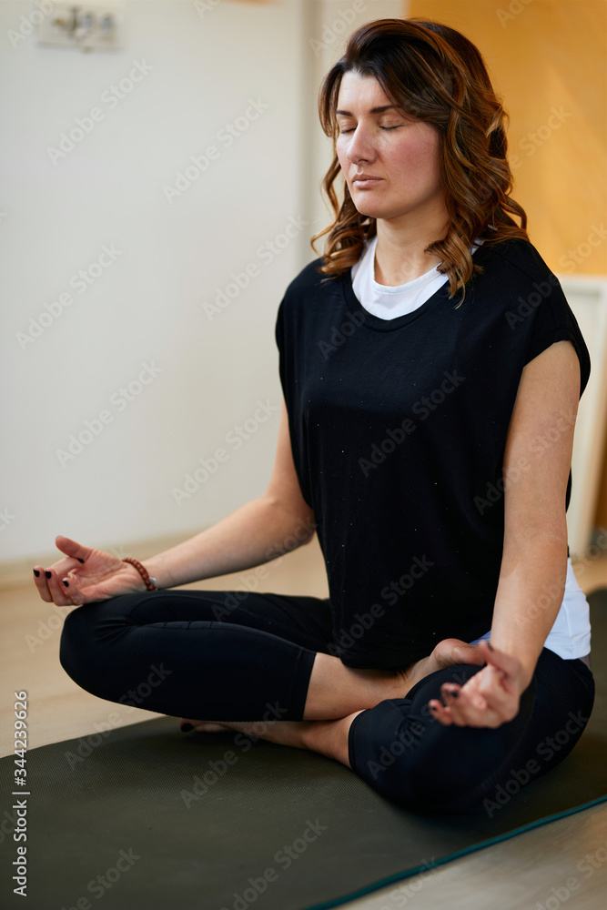 Close up of slim Caucasian yogi woman sitting on the mat at home in lotus position and meditating. Close up of slim Caucasian yogi woman sitting on the mat at home in lotus position and meditating.