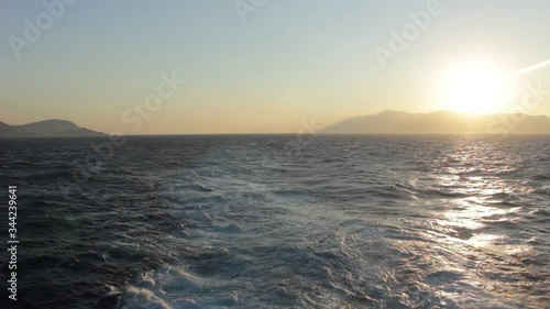 The propellers of the ship create whirlpools and the waves play with the rays of the departing sun. In the distance are two islands, one of which is ablaze with solar fire.