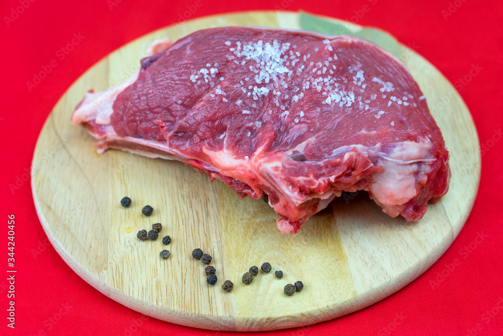 A piece of raw beef on a chopping Board, with pepper grains and salt