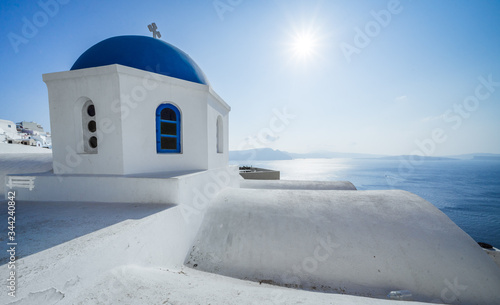 sun and blue dome orthodox church in Oia, Santorini island, Cyclades, Greece