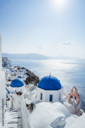Agios Spiridonas and Anastasi Church(blue dome) with tower bell in Oia, Santorini island, Cyclades, Greece