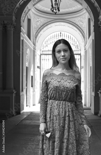 Portrait of a beautiful young woman with long hair and a lace dress with an Italian stone and marble neoclassical palace entrance in the background. Black and white.