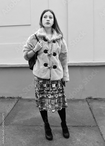 Portrait of a beautiful young woman with long hair and a synthetic fur in a city street. Black and white.