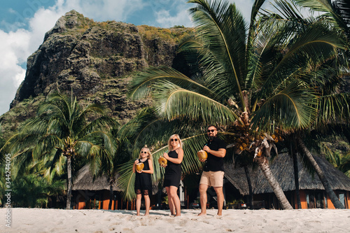 a stylish family in black clothes with coconuts in their hands on the beach of the island of Mauritius.Beautiful family on the island of Mauritius against the backdrop of mount Le Morne Brabant