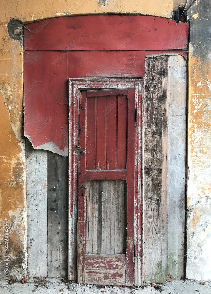 A old red wooden door on a ancient abandoned building.