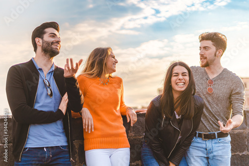 Fotografie Group of trendy young people chatting together standing on a small wall outdoors