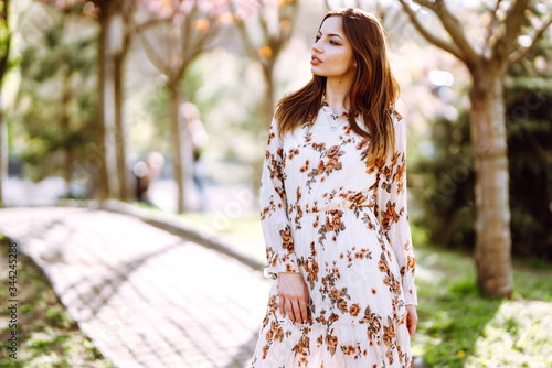 Beautiful young woman near the blooming spring tree. Attractive girl enjoying her time outside in park. Spring time.