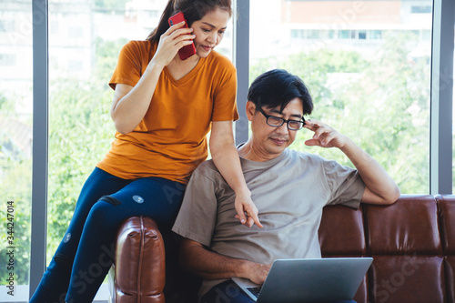 Senior couple are sitting on a sofa and looking at a laptop in order to buy things or discuss some task together