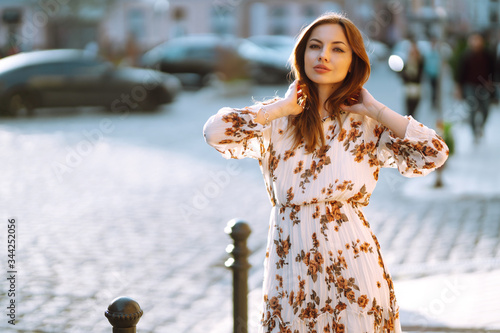 Fotografia The portrait of young stylish woman in fashion dress posing at sunset in the city