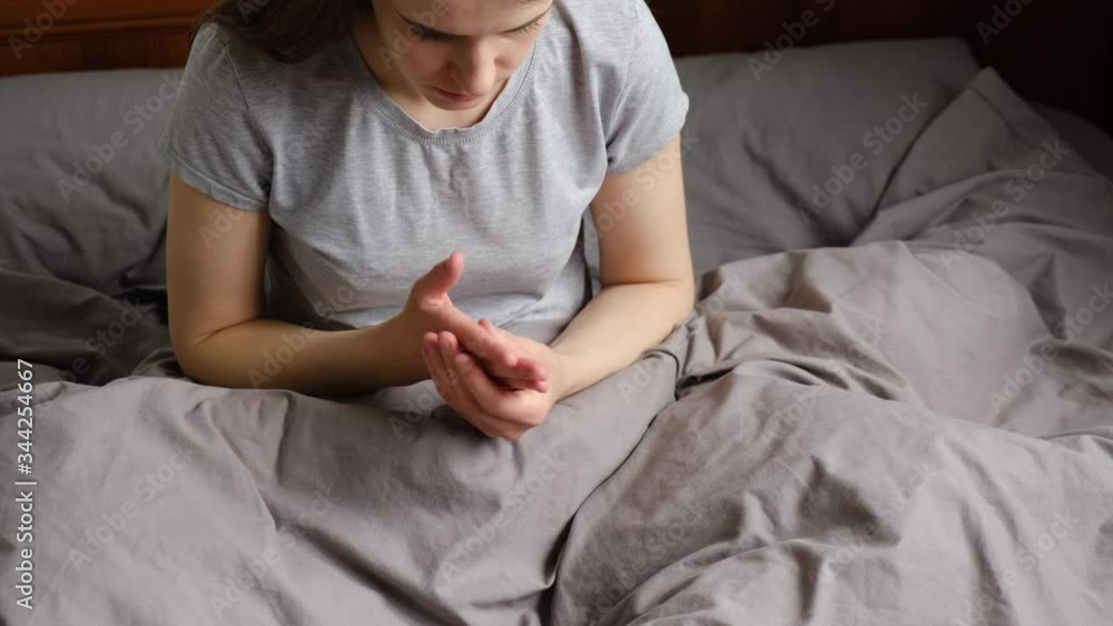 Tired young woman sitting on bed massaging hand suffering from