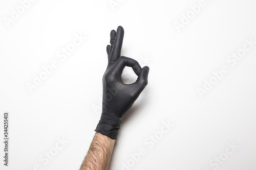 Medical glove in black on a white background. Hand showing okay sign.