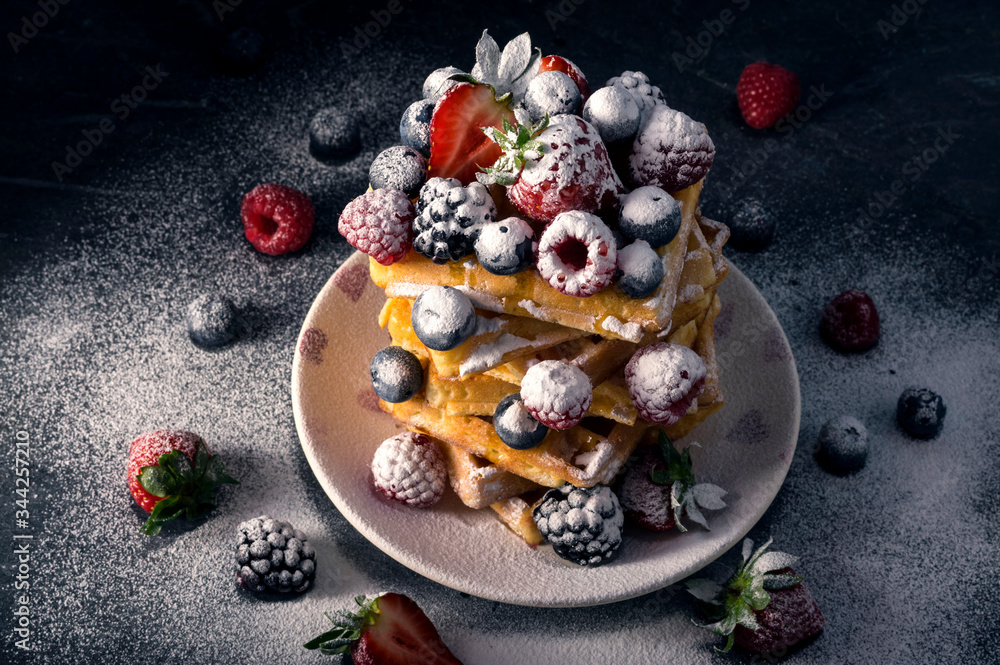 Traditional homemade Belgian waffles with fresh summer berries, blueberry raspberry, strawberry and blackberry dusted with icing sugar.