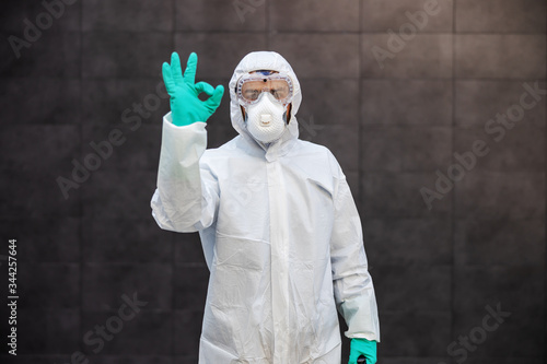 Portrait of man in sterile uniform and mask standing outdoors and showing okay sign. Surfaces are all sterilized from corona virus/ covid-19. photo