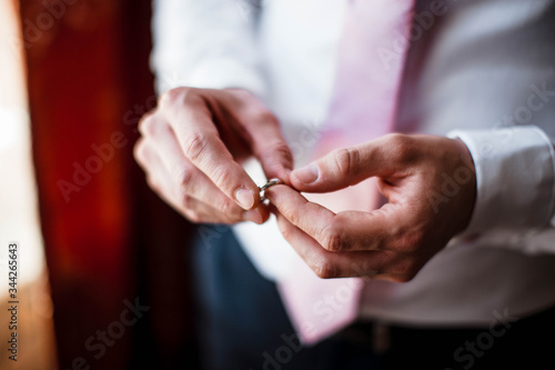 Closeup of groom puts a wedding ring on his finger. The groom holds a golden ring in his fingers.