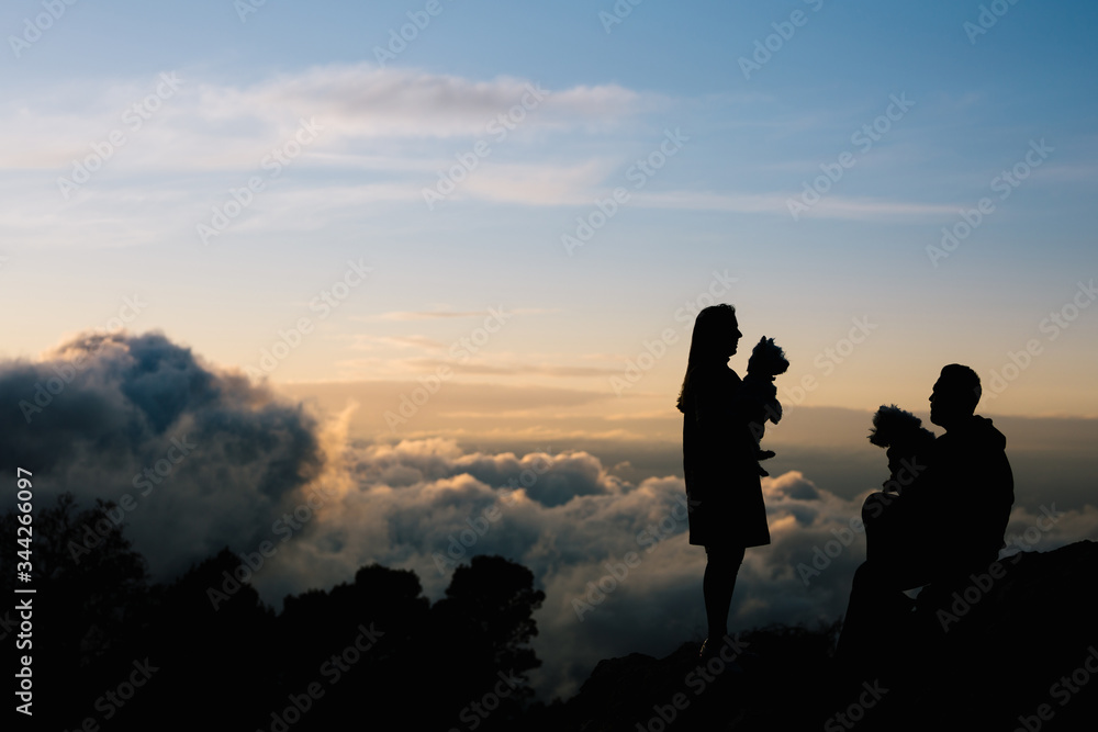 Silhouette of a woman and a man with their dogs in the cloud covered mountains